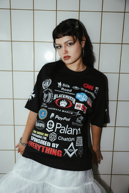 Sponsored by Everything black graphic T-shirt styled with a white skirt, front portrait against a tiled wall.