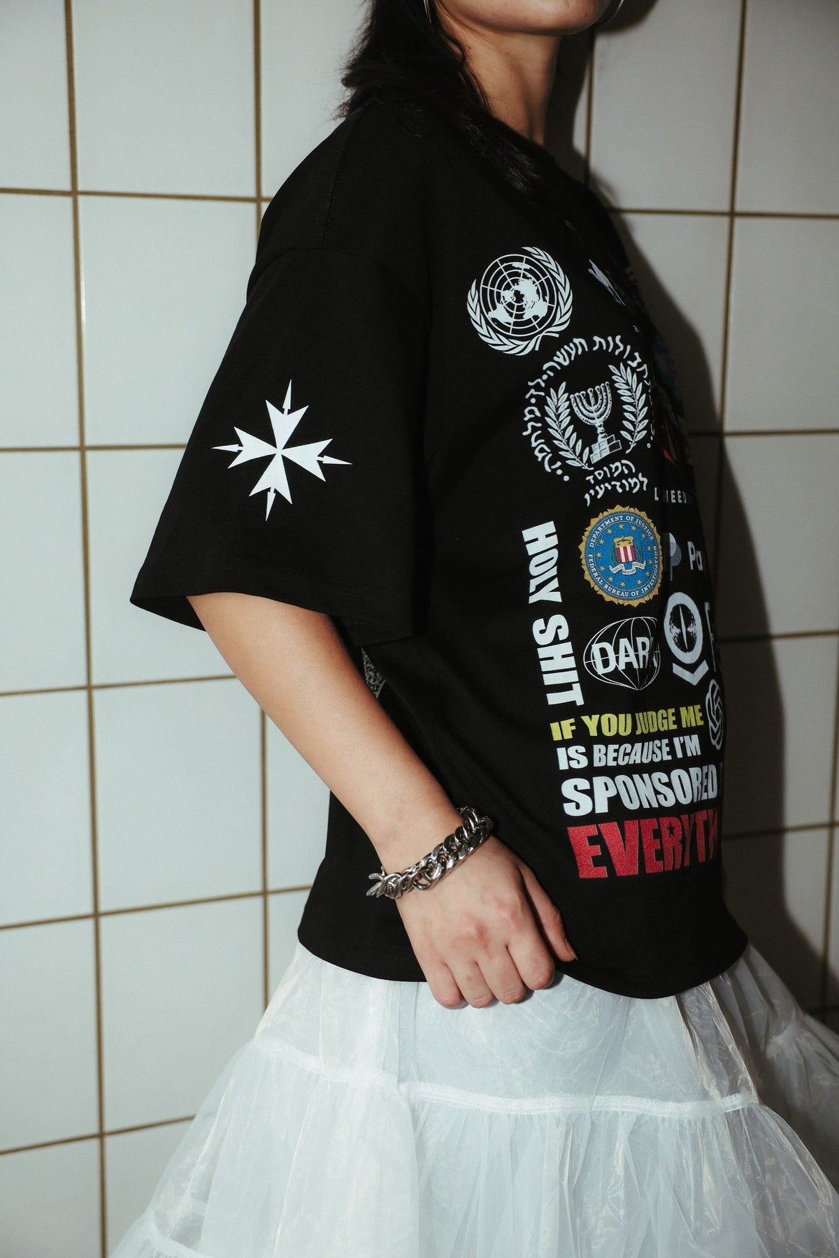 Sponsored by Everything black graphic T-shirt, close side view showing the sleeve cross and front print.